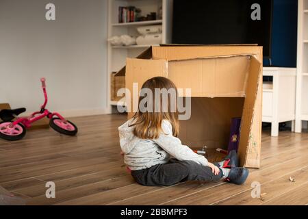 Kleines Kindermädchen, das mit einem Pappspielhaus spielt, während es in einem neuen Haus umzieht. Idee zu Lockdown-Aktivitäten. Stockfoto