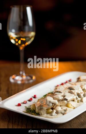 Hühnerfleisch auf geriebenem Gnocchi in Sahnesauce aus Pilzen und geräuchertem Käse auf dem Tisch mit Glas Weißwein Stockfoto