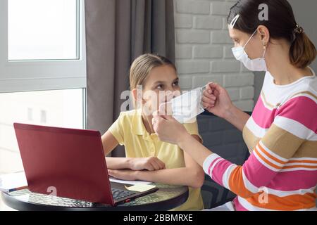 Das Mädchen zu Hause legt dem Kind eine medizinische Schutzmaske zu Stockfoto