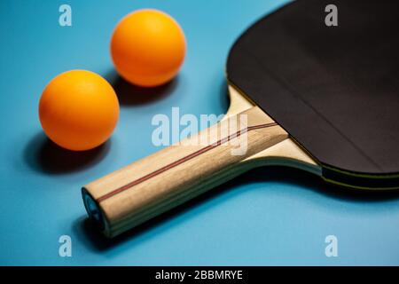 Nahaufnahme von Tischtennisschläger und zwei orangefarbenen Kugeln auf blauem Hintergrund, Sportkonzept Stockfoto