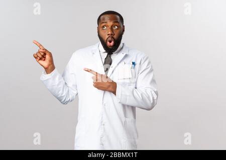 Covid19, Konzept für das Gesundheitswesen und die Klinik. Beeindruckt, sprachloser afroamerikanischer männlicher Arzt, der mit Krankenschwestern im Krankenhaus klatscht, sagt Wow, Look and Stockfoto