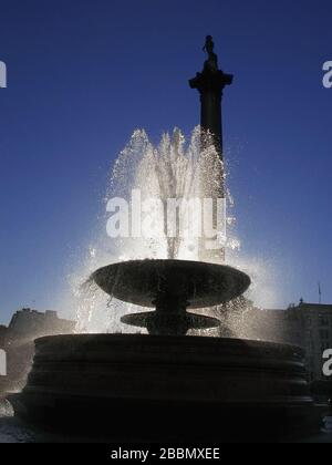 Nelsons Säule und Springbrunnen, Trafalgar Square, London, England, Großbritannien: Silhouette und sonniger Wasserstrahl mit Hintergrundbeleuchtung Stockfoto