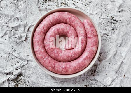 Hochwinkeliger Blick auf eine gerollte Botifarra, eine für Katalonien typische Schweinefleischwurst in Spanien, auf einem Teller, auf einem weißen texturierten Textilhintergrund Stockfoto