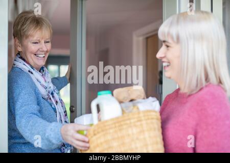 Weibliche Nachbarin Hilft Seniorin Beim Einkaufen, Während Sie Sich Während Coronavirus Selbst Isoliert Stockfoto