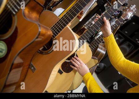 Frau, die sich für eine neue Gitarre im Instrumentenshop für ihr liebliches Hobby oder ihre Freizeit, ihr Shopping-Konzept, entscheidet Stockfoto