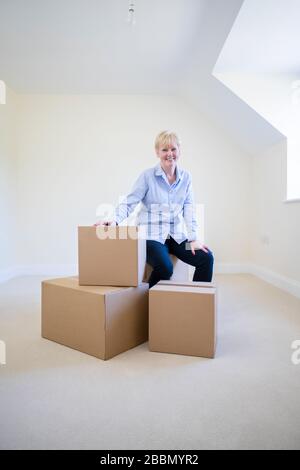 Portrait Der Älteren Frau, Die Im Ruhestand Auf Boxen In New Home Am Beweglichen Tag Sitzt Stockfoto
