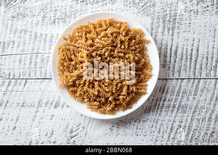 Vollkornspelz geformte Fusilli auf Platte auf weißem Holzhintergrund. Stockfoto