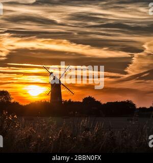 Bircham Windmühle mit dramatischem Himmel bei Sonnenuntergang mit Weizenfeldern im Vordergrund in Norfolk England Stockfoto