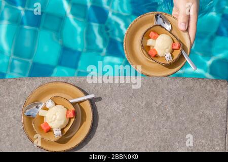 Zwei Eiscreme werden in der Nähe des Pools serviert. Desserts auf dem blauen Pool-Wasserhintergrund. Yin und Yang Konzept. Ein Paar frühstücken in der Nähe des Pools. Stockfoto