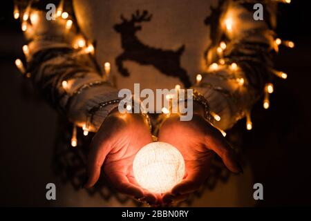 Mädchen in einem Pullover mit einem Hirsch hält leuchtenden Ball. Weihnachts-Vorstellung. Frohe Neujahrsfeier. Stockfoto