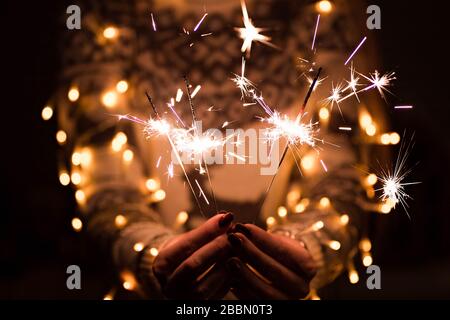 Mädchen in einem Pullover mit einem Hirsch hält brennende Sparklers fest. Weihnachts-Vorstellung. Frohe Neujahrsfeier. Stockfoto