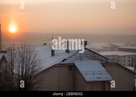 Fantastischer rosafarbener Winteraufgang. Schöner Weihnachtshintergrund. Blick vom Fenster auf die mit Schnee bedeckten Dächer. Wintermorgen. Stockfoto