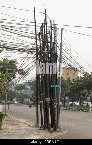 Jakarta, Indonesien - 13. Juli 2019: Pole, die mit einem Gewirr aus schwarzen unterirdischen Stromkabeln beladen sind, auf den Straßen von Zentral-Jakarta. Stockfoto