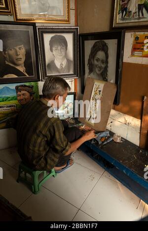 Jakarta, Indonesien - 13. Juli 2019: Ein lokaler Maler und Karikaturist malt in seinem kleinen Atelier einen blühenden Zweig mit Vögeln mit Acrylfarben. Stockfoto