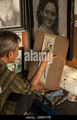 Jakarta, Indonesien - 13. Juli 2019: Ein lokaler Maler und Karikaturist malt in seinem kleinen Atelier einen blühenden Zweig mit Vögeln mit Acrylfarben. Stockfoto