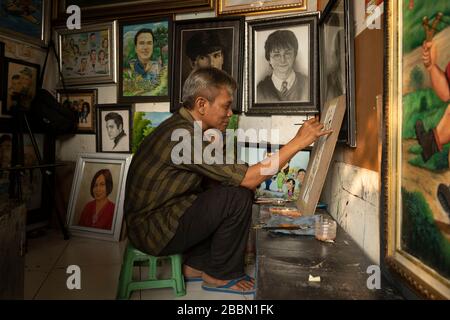 Jakarta, Indonesien - 13. Juli 2019: Ein lokaler Maler und Karikaturist malt in seinem kleinen Atelier einen blühenden Zweig mit Vögeln mit Acrylfarben. Stockfoto