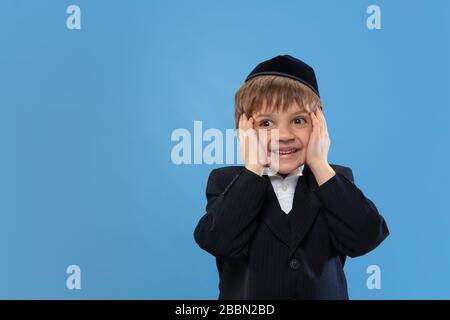 Erstaunt. Porträt eines jungen orthodoxen jüdischen Jungen isoliert auf blauem Studiohintergrund. Purim, Business, Festival, Urlaub, Kindheit, Feier Pesach oder Passah, judaismus, Religionskonzept. Stockfoto