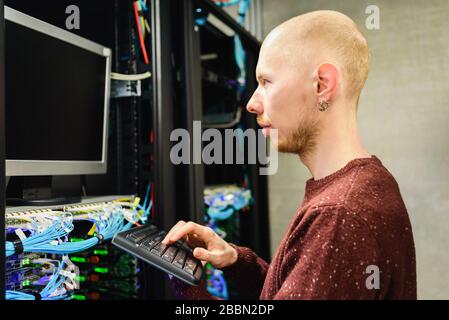 Man-Rechenzentrumstechniker, der Serverwartung durchführt. Verwenden der Tastatur zum Konfigurieren der Infrastruktur Stockfoto