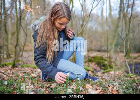 Ein 11-jähriges Mädchen zieht eine kleine weiße Blume in den Wald Stockfoto