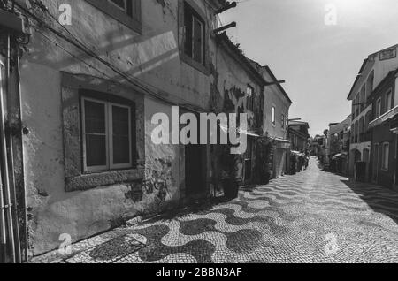 Die windige, schmale Kopfsteinpflaster führt zwischen traditionellen verfallenen und renovierten Häusern aus weiß getünchten Stein in Cascais Portugal. Stockfoto