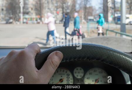 Blick aus dem Auto, Hand des Mannes am Lenkrad des Autos, befindet sich gegenüber der Fußgängerampel und Fußgänger über die Straße Stockfoto