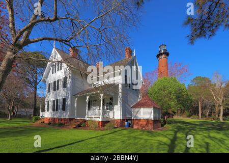 Keeper Quarters vor der roten Ziegelstruktur des Currituck Beach Lighthouse mit Quellbäumen im Currituck Heritage Park bei Corolla Stockfoto