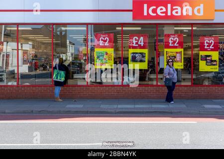 Menschen, die zwei Meter voneinander entfernt stehen oder soziale Distanzierungen haben, während sie Schlange stehen, um in einem Supermarkt in Island Lebensmittel zu kaufen Stockfoto