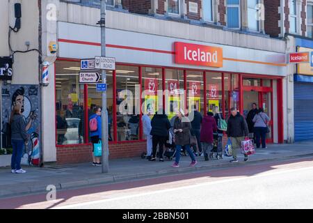 Menschen, die zwei Meter voneinander entfernt stehen oder soziale Distanzierungen haben, während sie Schlange stehen, um in einem Supermarkt in Island Lebensmittel zu kaufen Stockfoto