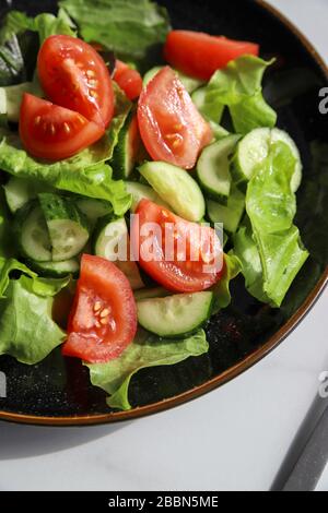 Frischer Detox-Salat im Sommer mit Tomaten, Gurke, Romain-Salat und Olivenöl auf Marmorgrund. Gesunde Ernährung für Veganer oder Vegetarier, Top V Stockfoto