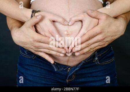 Die Hände des Vaters und der Mutter auf dem schwangeren Bauch der Frau Zeigt die Herzform an Stockfoto