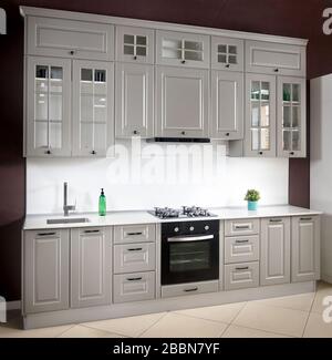 Innenbereich der weißen und grauen Küche, horizontal. Luxuriöse, moderne Einbauküche mit Glaselementen Stockfoto