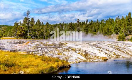 Heißes Wasser aus dem länglichen Geyser, das im oberen Geyser-Becken entlang des Continental Divide Trail in Yellowstone in den Firehole River fließt Stockfoto