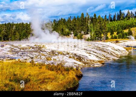 Heißes Wasser aus dem länglichen Geyser, das im oberen Geyser-Becken entlang des Continental Divide Trail in Yellowstone in den Firehole River fließt Stockfoto