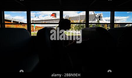 Chinesischer Schatten in einem Bus vor dem Kreuzfahrtschiff RMS Queen Mary II und dem Place des Canotiers. Stockfoto