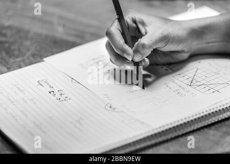 Die Hand eines Lehrers, der einen Bleistift hält und eine mathematische Gleichung (Formel) in einem Lehrbuch aufschreibt. Schwarz und Weiß. Stockfoto