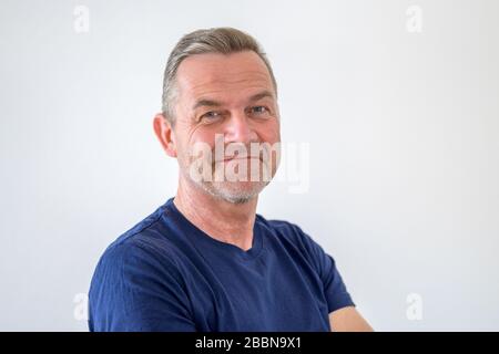Lächelnder, attraktiver Mann mittleren Alters in lässigem blauem T-Shirt im Kopf- und Schulterporträt auf Weiß mit Kopffarraum Stockfoto
