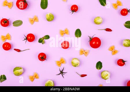 Bunte Nudelzutaten aus Kirschtomaten, brussel-spross, Farfalle und Pfeffer auf pinkfarbenem Hintergrund. Kochkonzept. Stockfoto