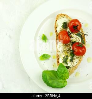 Konzept der gesunden Ernährung. Eine Scheibe Brot mit frischem Mozzarella-Käse, Tomaten und Basilikumblättern auf weißem Teller. Draufsicht, Kopierbereich. Stockfoto