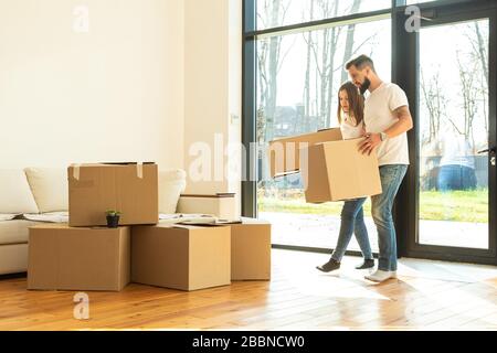 Das junge Paar zieht in ein neues Haus, die Familie trägt nach dem Kauf eines Hauses Kisten mit Sachen. Stockfoto