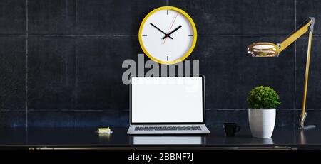 Laptop auf dem Schreibtisch mit Werk, Schreibtischlampe, gelber Wanduhr und 3D-Rendering aus schwarzem Beton Stockfoto