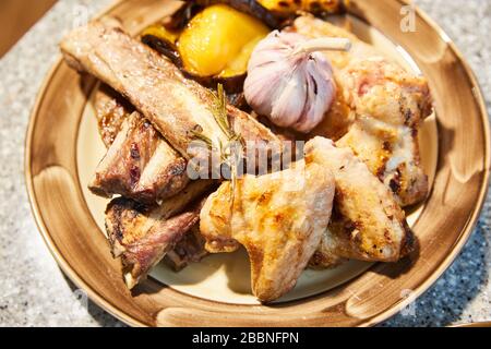 Hammelrippen mit Thymianzweig, Hühnerflügel, Knoblauch, gelber süßer Pfeffer stehen auf einem Teller, nah oben Stockfoto