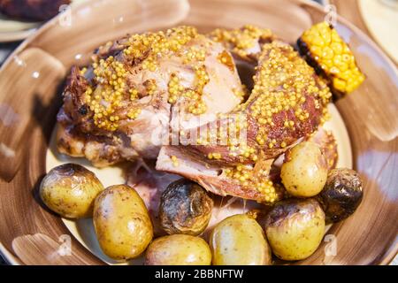 Das große Stück des gegrillten, gedämpften Schweinefleisches mit Senfsauce liegt auf einem Teller mit Kartoffeln und Mais, saftigem Fleisch Stockfoto