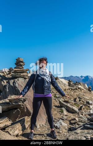 Junge Frau mit Palmen unten auf der Suche nach der Energie der Erde. Meditierend vor einer Steinpyramide. Eggishorn-Terrasse, Ort der Energie und Kraft Stockfoto