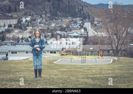 Trauriges Mädchen, das während der Coronavirus-Pandemie 2020 vor einem geschlossenen Spielplatz steht, der die Straßen der Stadt in Kanada überblickt Stockfoto