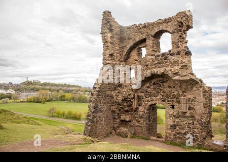 Die Ruine der St Anthony's Chapel im Holyrood Park mit Calton Hill im Hintergrund, die früh an einem übergiebelten Tag in Edinburgh fotografiert wurde Stockfoto