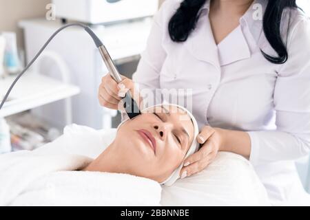 Nahaufnahme des Kosmetologen, der das Verfahren zum Peeling des Gesichts an eine reife Frau im Schönheitssalon hält Stockfoto