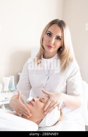 Porträt der attraktiven Schönheit professionell im Labormantel, die Gesichtsmassage zum Glätten von Falten reifer Frauen macht Stockfoto