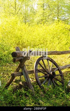 Altes Wagenrad neben einem Holzzaun auf dem Land. Stockfoto