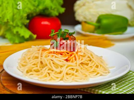 Pasta mit Fleischbällchen in Tomatensauce auf dem weißen Teller mit frischem Gemüse auf dem Hintergrund Stockfoto