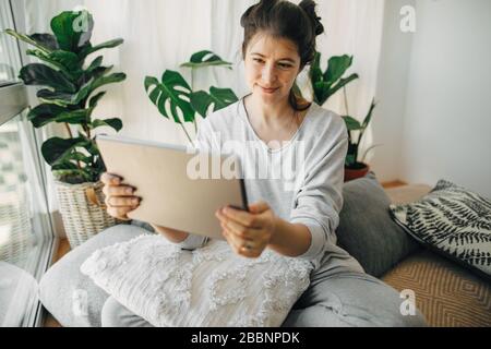 Hipper-Mädchen mit Tablet, Arbeit oder Chat von zu Hause aus während der Quarantäne im modernen Raum. Bleiben Sie zu Hause bleiben Sie sicher. Isolierung zu Hause zur Vermeidung von Viren e Stockfoto